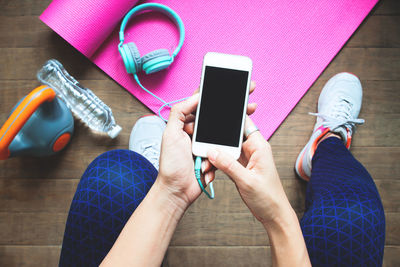 Low section of woman using mobile phone by exercising equipment on floor at home