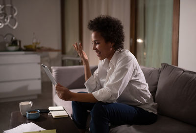 Happy ethnic freelancer making online call on sofa