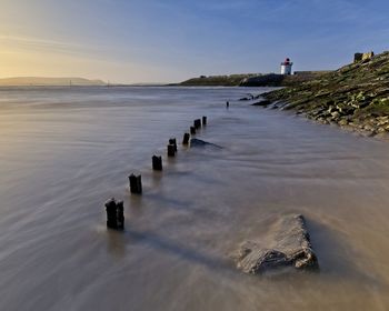 Wooden posts in sea against sky