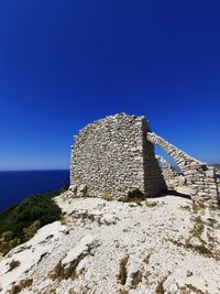 Stone wall by sea against clear blue sky