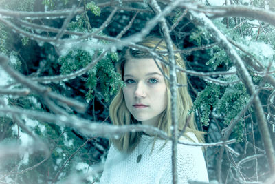 Portrait of teenage girl standing amidst frozen tree branches in forest