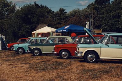 Cars on road by field against sky