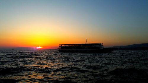 Boat sailing in sea against clear sky during sunset