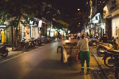 Rear view of woman collecting garbage in container on illuminated street at night