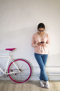 Smiling woman using mobile phone while standing by bicycle at home