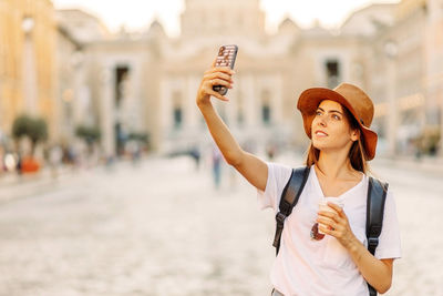 Portrait of smiling young woman taking selfie in city