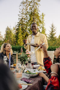 Smiling man having food with friends during dinner party in back yard