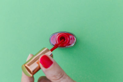 Fingers of a woman with red nail and nail polish on a green background