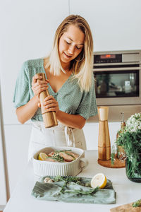 Young european woman grinding pepper in tray with quail for roasting