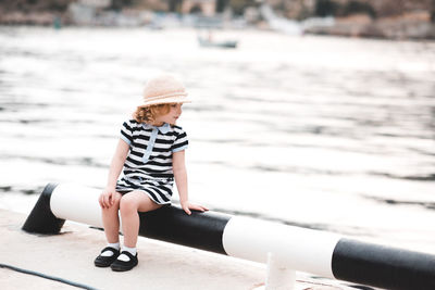 Cute girl looking at sea while sitting on pipe