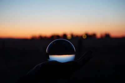 Cropped hand holding crystal ball against clear sky during sunset