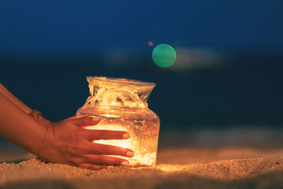 Close-up of woman hand holding illuminated lighting equipment in glass jar at beach during night
