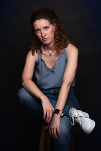 Portrait of young woman standing against black background