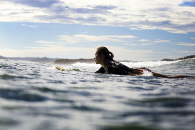 Side view of female surfer lying on surfboard in sea