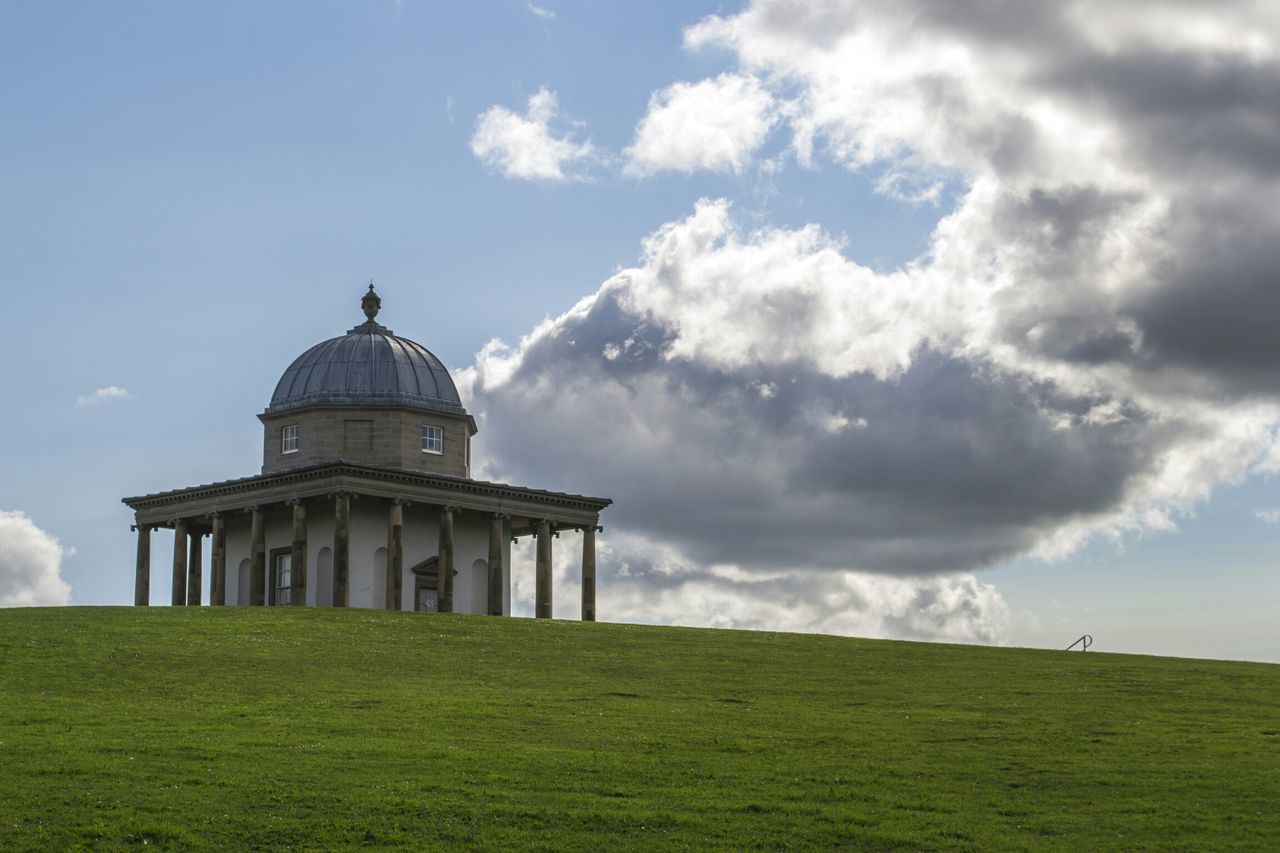 sky, architecture, built structure, grass, building exterior, religion, place of worship, spirituality, cloud - sky, church, cloudy, dome, cross, cloud, low angle view, field, green color, travel destinations