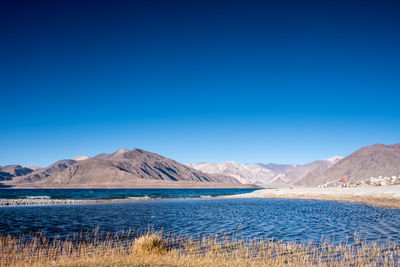 Scenic view of lake and mountains against clear blue sky