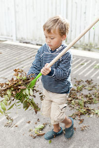 Boy playing with fallen dry leaves at back yard