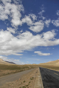 A flat, newly built wide asphalt road leads to the beautiful mountains in the distance