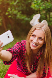 Portrait of smiling young woman using mobile phone in park