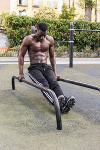 Determined black sportsman doing parallel bar dips on parallel bars during workout on sports ground