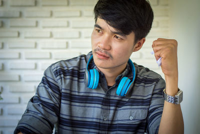 Portrait of young man looking away against wall