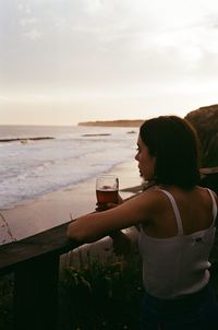 Woman drinking coffee at sea shore against sky