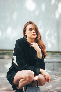 Portrait of beautiful young woman crouching outdoors