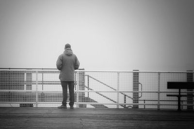 Man standing on railing against clear sky