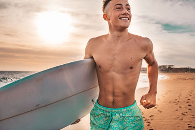 Full length of shirtless man standing at beach against sky