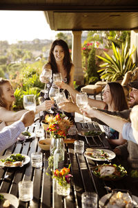 Happy friends toasting wineglasses at dining table on porch