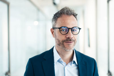 Confident businessman wearing eyeglasses in corridor at office