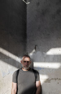 Portrait of adult man standing against old wall with sunlight  and shadow