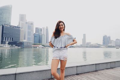 Portrait of young woman standing against river in city