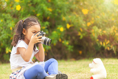 Girl photographing with toy while sitting on land