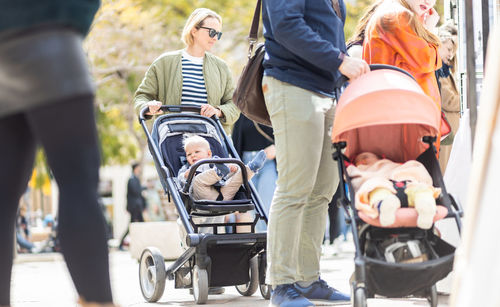 Mother walking and pushing his infant baby boy child in stroller in crowd of people wisiting sunday