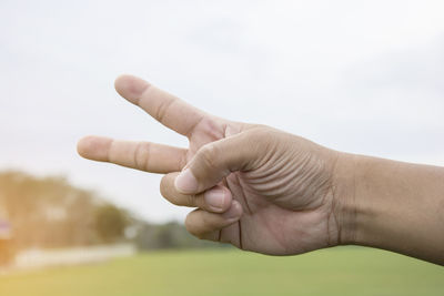 Close-up of hand gesturing against sky