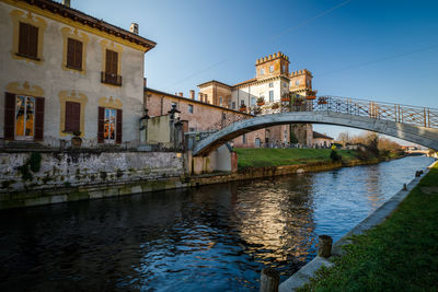 Bridge over river by buildings against sky