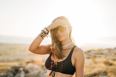 Woman wearing sunglasses while standing at beach during sunset