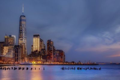 Illuminated one world trade center by buildings against sky at night