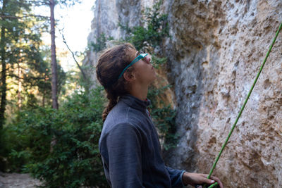 Side view of hiker holding rope while standing by rock