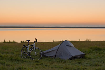 Bicycle on grassy field at campsite by lake against clear sky during sunset