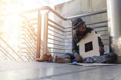 Full length of homeless person sitting on footpath