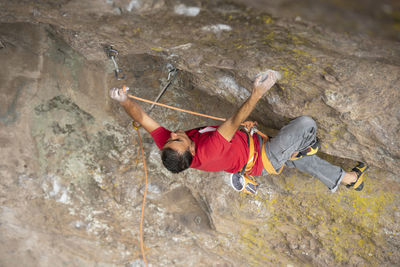 One man wearing red clips a carabiner with a rope while rock climbing