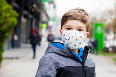 Portrait of smiling boy wearing protective face mask in the city during covid-19 pandemic.