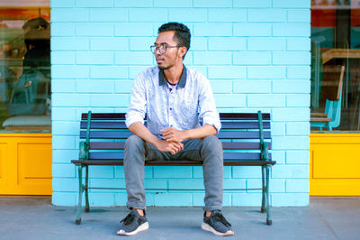 Full length of young man sitting on bench in city