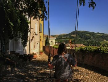 Rear view of woman sitting on swing against clear blue sky