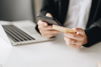 Midsection of businesswoman using mobile phone while holding credit card