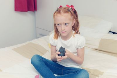 Portrait of cute girl using mobile phone while sitting on sofa at home