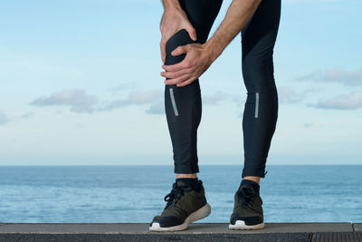 Low section of man standing by sea against sky