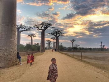 Boy playing with umbrella against sky during sunset